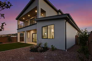 Back of house at dusk featuring a fenced backyard, a patio, a balcony, and stucco siding