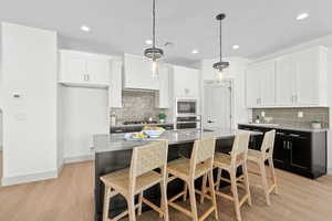 Dual tone kitchen with two tone cabinets, a breakfast bar, hanging light fixtures, stainless steel appliances, and light wood finished floors