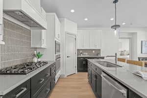 Dual tone kitchen featuring dual tone cabinets, light wood finished floors, stainless steel appliances, decorative light fixtures, and light stone counters