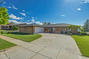 Ranch-style house with an attached garage, a front yard, a chimney, driveway, and brick siding
