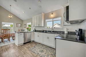 Kitchen featuring dark countertops, a peninsula, tasteful backsplash, light wood-type flooring, and stainless steel dishwasher