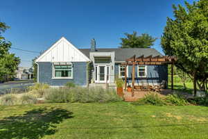 Rear view of house featuring a pergola, brick siding, board and batten siding, a yard, and a chimney