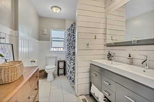 Full bath with a textured ceiling, wood walls, vanity, tile patterned flooring, and a wainscoted wall
