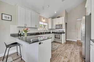 Kitchen with a peninsula, stainless steel appliances, decorative backsplash, white cabinetry, and light wood-type flooring