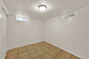 Basement with a textured ceiling, light tile patterned floors, and wood walls