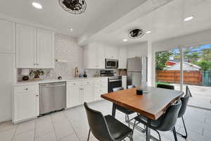 Kitchen with stainless steel appliances, decorative backsplash, light countertops, white cabinets, and recessed lighting