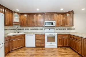 Kitchen featuring white appliances, tasteful backsplash, light wood-style flooring, glass insert cabinets, and recessed lighting