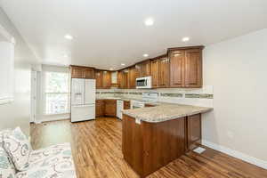 Kitchen featuring tasteful backsplash, a peninsula, white appliances, light wood-type flooring, and recessed lighting