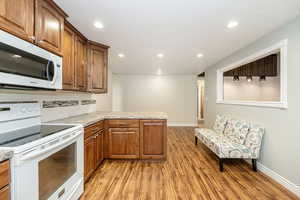 Kitchen with white appliances, light wood-style flooring, a peninsula, tasteful backsplash, and recessed lighting