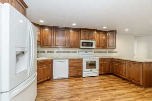 Kitchen featuring white appliances, light wood-style flooring, decorative backsplash, a peninsula, and recessed lighting