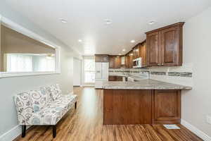 Kitchen with tasteful backsplash, white appliances, a peninsula, wood finished floors, and recessed lighting