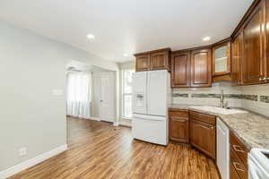 Kitchen featuring decorative backsplash, white appliances, light wood-style flooring, glass insert cabinets, and light stone countertops