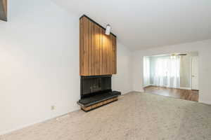 Unfurnished living room featuring a large fireplace, carpet flooring, lofted ceiling, and ceiling fan