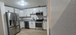 Kitchen with stainless steel appliances, light wood finished floors, white cabinetry, and light stone countertops