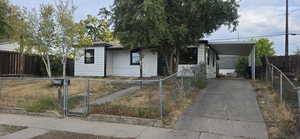 View of front of home with a fenced front yard, an attached carport, and driveway