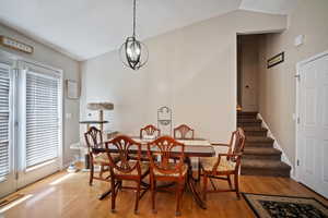 Dining room with vaulted ceiling, light wood-type flooring, a chandelier, and stairs