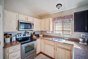 Kitchen featuring light brown cabinets, appliances with stainless steel finishes, vaulted ceiling, and dark countertops