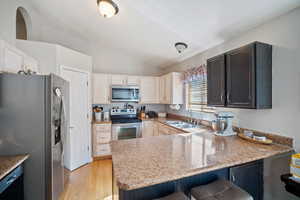 Kitchen featuring stainless steel appliances, a peninsula, lofted ceiling, light wood-style flooring, and a kitchen bar