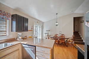 Kitchen featuring vaulted ceiling, light wood-style floors, stainless steel dishwasher, a peninsula, and hanging light fixtures