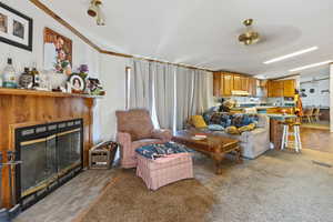 Living area featuring a fireplace with flush hearth, light carpet, and crown molding