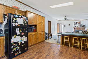 Kitchen with freestanding refrigerator, ornamental molding, a kitchen breakfast bar, dark wood-style floors, and brown cabinetry