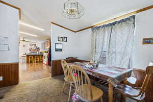 Dining space with wooden walls, a wainscoted wall, crown molding, a chandelier, and carpet flooring