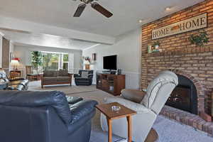 Living area with a textured ceiling, a brick fireplace, carpet flooring, ceiling fan, and crown molding