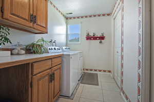 Washroom featuring light tile patterned flooring, cabinet space, and washing machine and clothes dryer