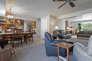 Living area with a textured ceiling, light carpet, light tile patterned floors, ceiling fan, and a wainscoted wall