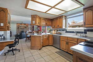 Kitchen with brown cabinets, tasteful backsplash, a peninsula, dishwasher, and light tile patterned floors