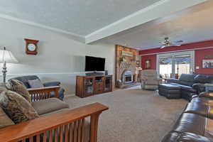 Carpeted living room featuring a fireplace, crown molding, a ceiling fan, and a textured ceiling
