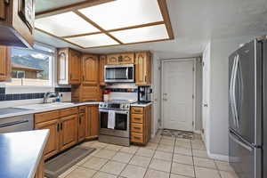 Kitchen with stainless steel appliances, brown cabinets, light tile patterned flooring, tasteful backsplash, and a textured ceiling