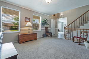 Sitting room featuring carpet, wallpapered walls, stairway, and crown molding