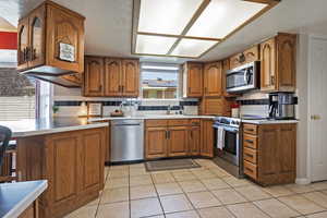 Kitchen featuring brown cabinets, backsplash, a peninsula, and light tile patterned floors