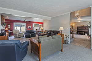 Carpeted living room with a textured ceiling, a chandelier, wallpapered walls, a ceiling fan, and crown molding