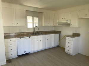 Kitchen with dishwasher, dark countertops, light wood finished floors, white cabinets, and under cabinet range hood