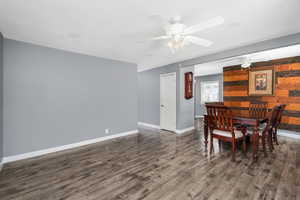 Dining area with dark wood finished floors, a ceiling fan, and wooden walls