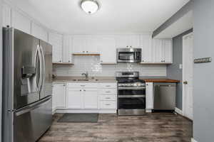 Kitchen featuring appliances with stainless steel finishes, white cabinetry, backsplash, and dark wood-style floors