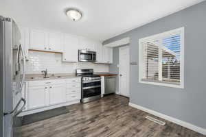 Kitchen with stainless steel appliances, backsplash, white cabinets, dark wood-style flooring, and light countertops