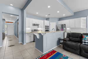 Kitchen with light tile patterned floors, decorative backsplash, a kitchen bar, white cabinets, and recessed lighting