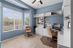 Office space with light wood finished floors, ceiling fan, and built in study area