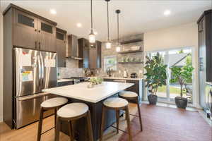 Kitchen with appliances with stainless steel finishes, light wood finished floors, backsplash, a kitchen breakfast bar, and light countertops