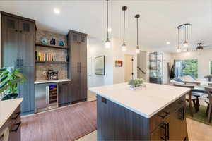 Kitchen featuring a kitchen island, light wood-type flooring, wine cooler, recessed lighting, and hanging light fixtures