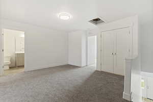 Unfurnished bedroom featuring light colored carpet, ensuite bathroom, and a closet