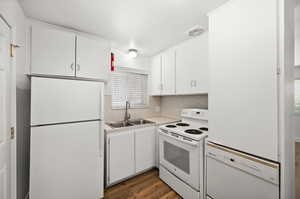 Kitchen featuring white appliances, light countertops, white cabinets, dark wood-style floors, and backsplash