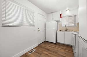 Kitchen with white appliances, white cabinetry, light countertops, dark wood finished floors, and tasteful backsplash