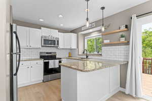 Kitchen featuring a peninsula, stainless steel appliances, white cabinetry, backsplash, and recessed lighting
