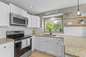 Kitchen featuring stainless steel appliances, white cabinets, light wood-style floors, recessed lighting, and light stone countertops