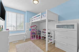 Bedroom with a wainscoted wall, light wood finished floors, and a textured ceiling