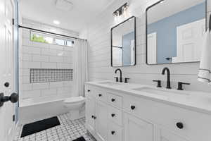 Bathroom featuring double vanity, shower / bathtub combination with curtain, wood walls, and mail area